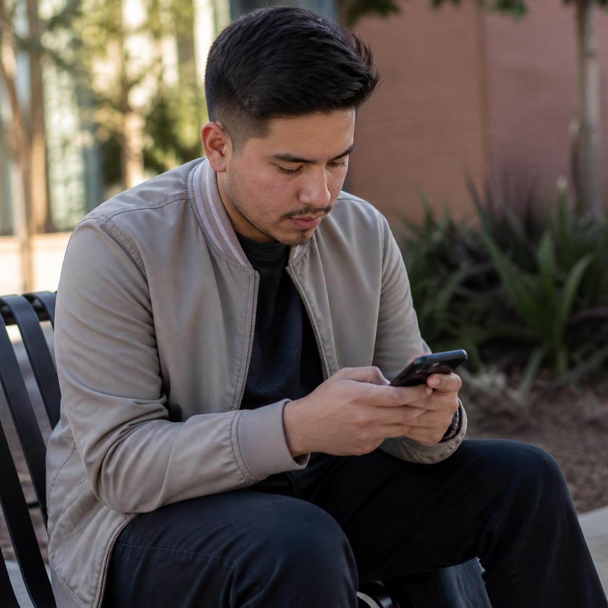 A young man on a bench typing a sincere check-in text message.