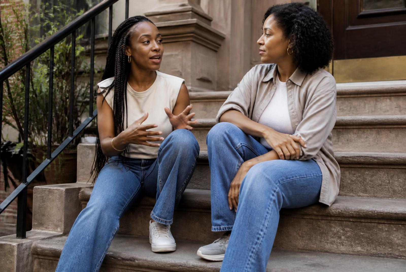Two friends sitting together on apartment steps — one talking, one genuinely listening.